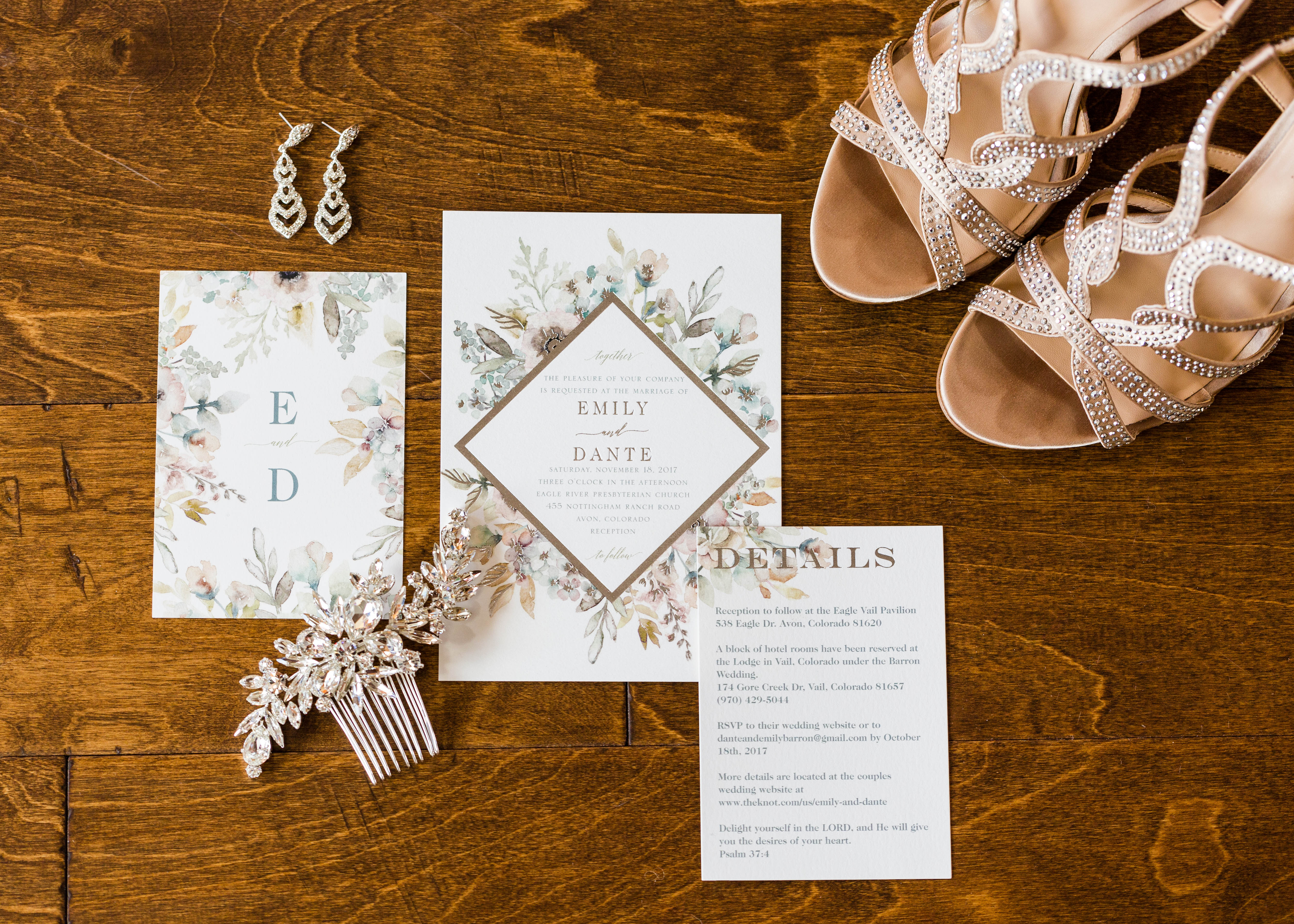 Bride's crystal studded shoes, earrings and floral invitations are nicely arranged on a wood floor