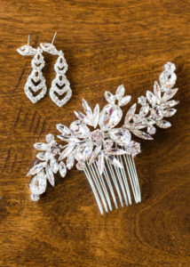 Bride's crystal hair piece and earrings lay gently on the wood floor