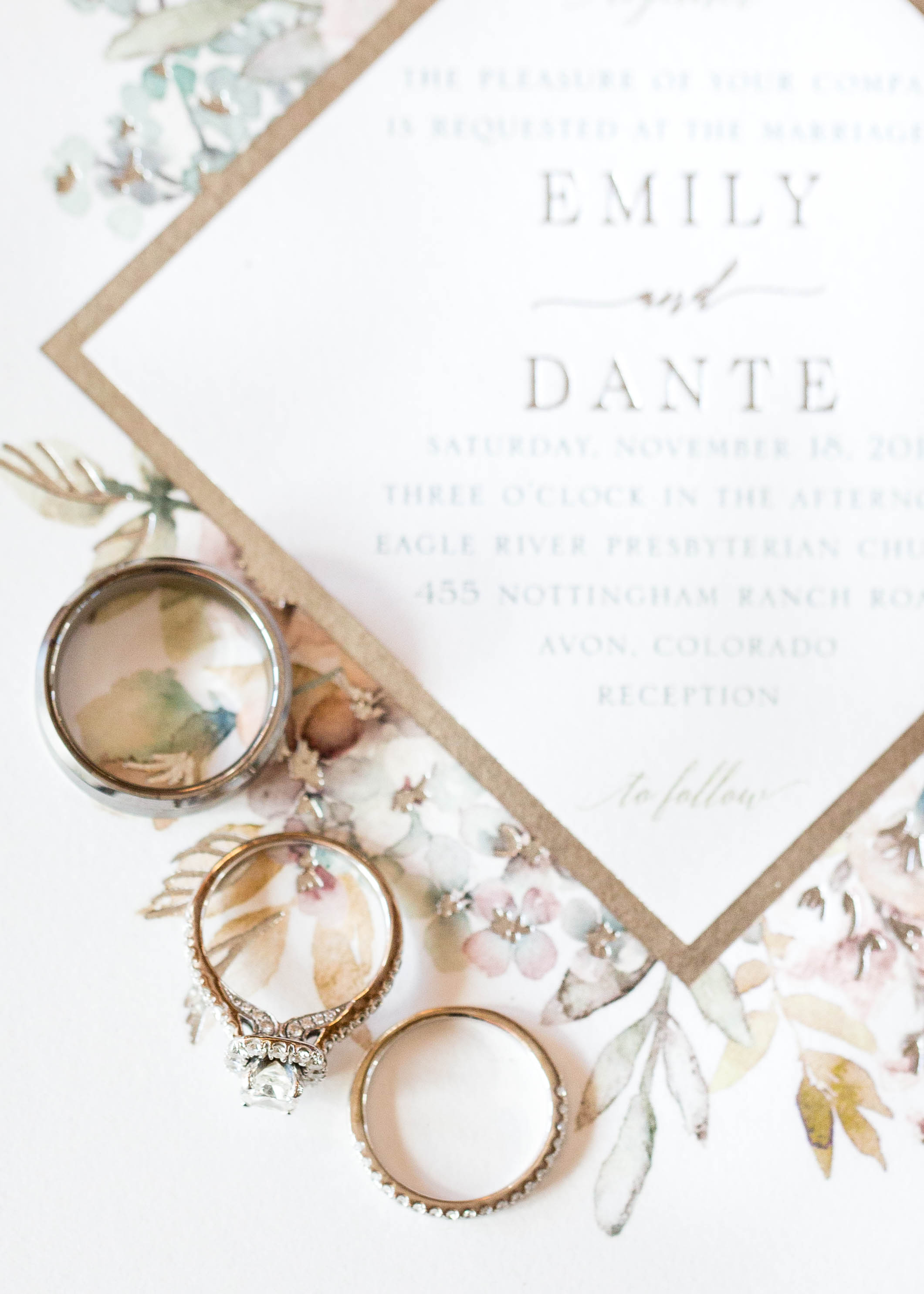 bride and groom's rings arranged diagonally on a gold and pastel floral invitation