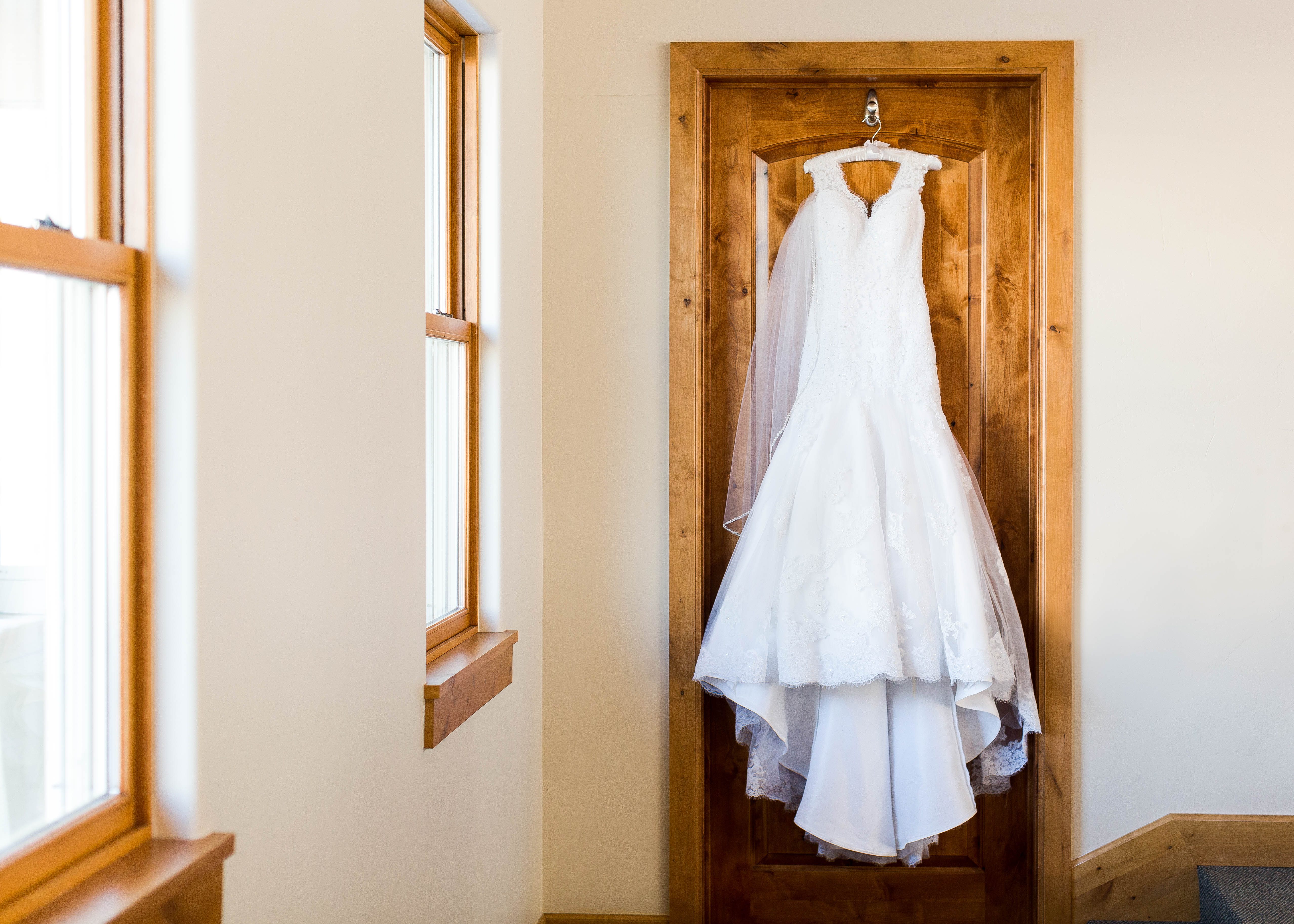 Elegant beaded sheath style wedding dress hangs from a wooden door