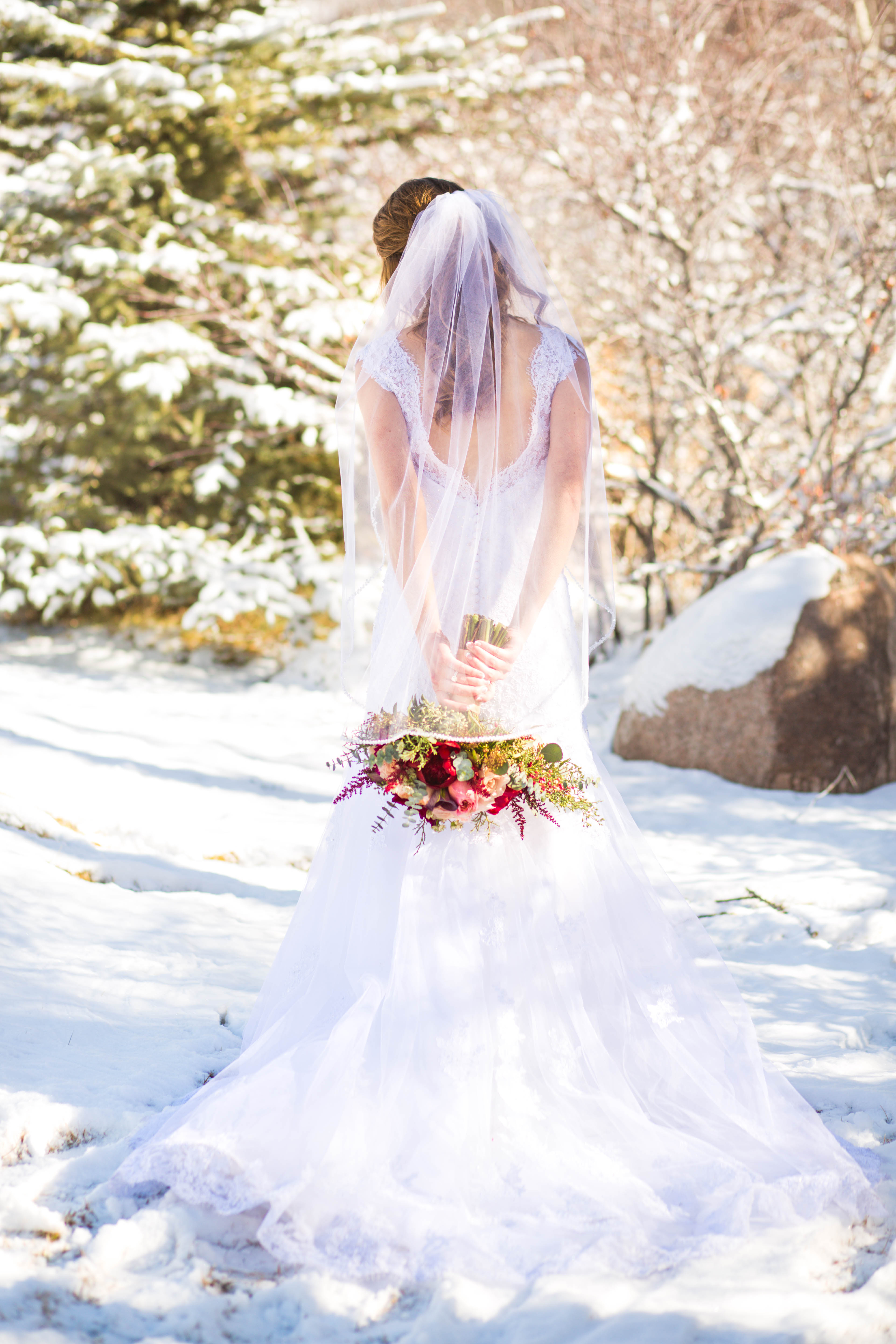 Bride stands in the snow while holding her bouquet behind her back
