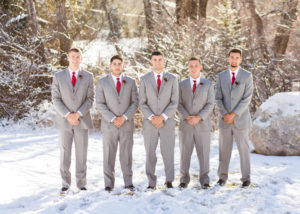 groom stands with groomsmen in the snow