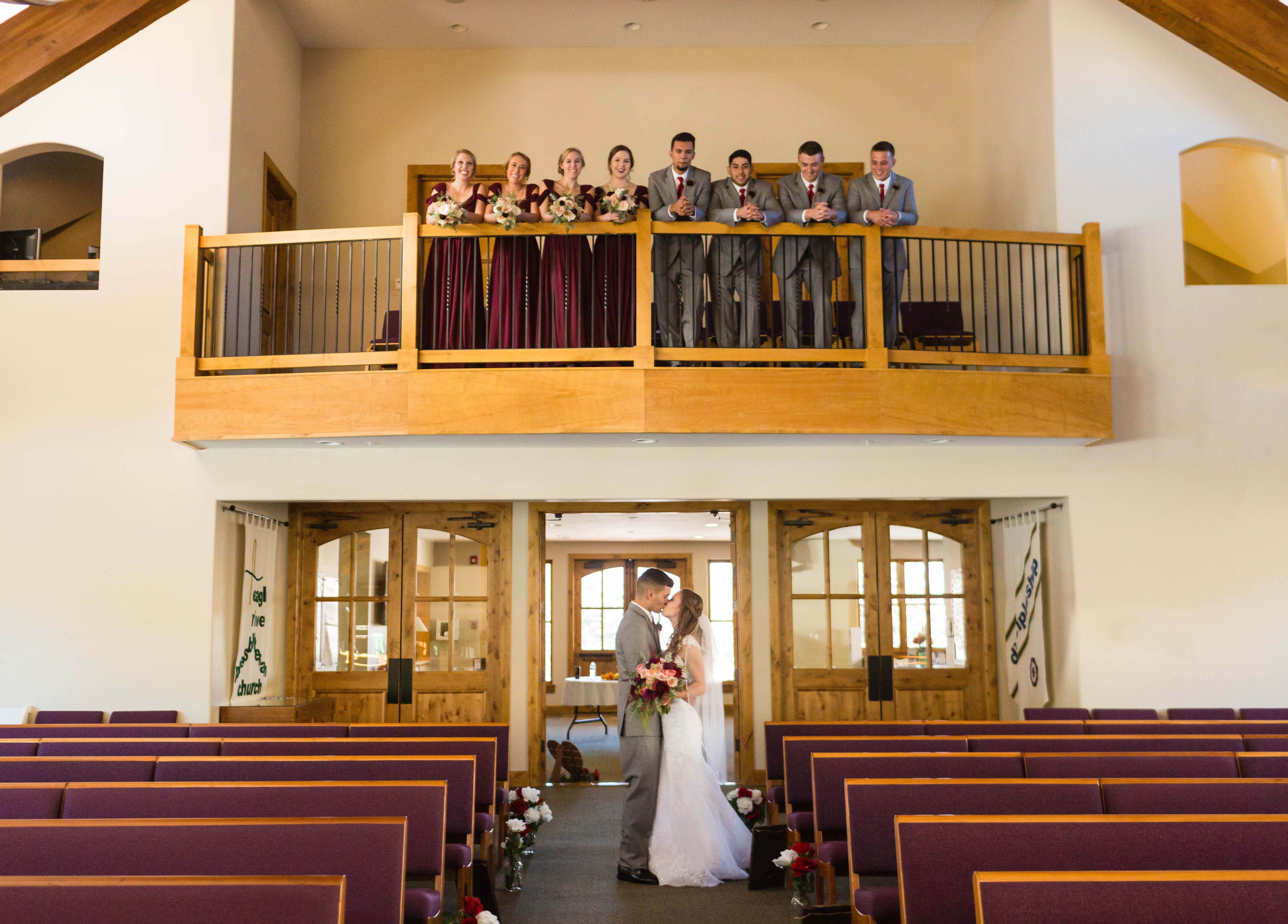 wedding party gaze down at bride and groom from church balcony