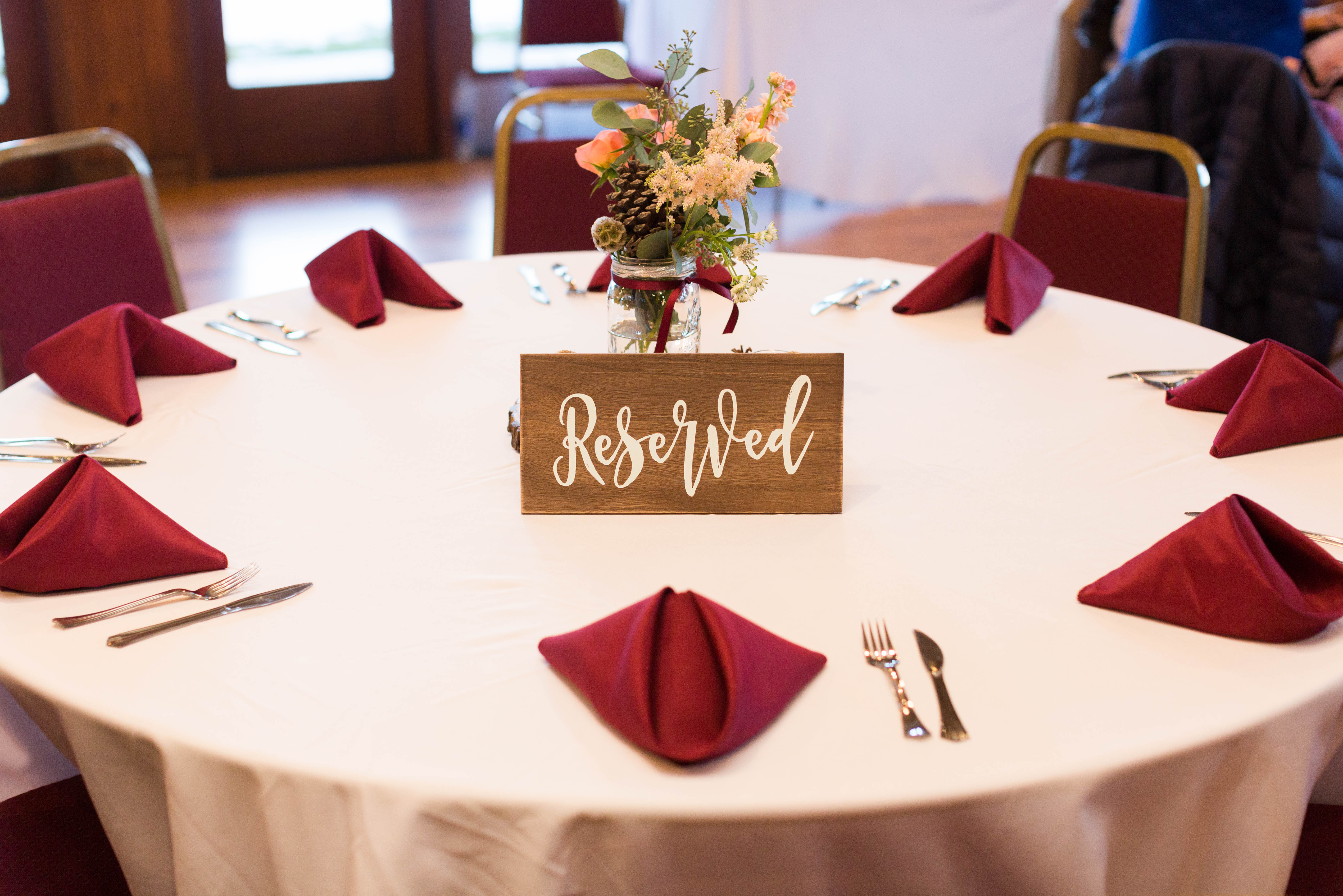 reception table decorated with white table cloth, burgundy napkins and a peach floral arrangement