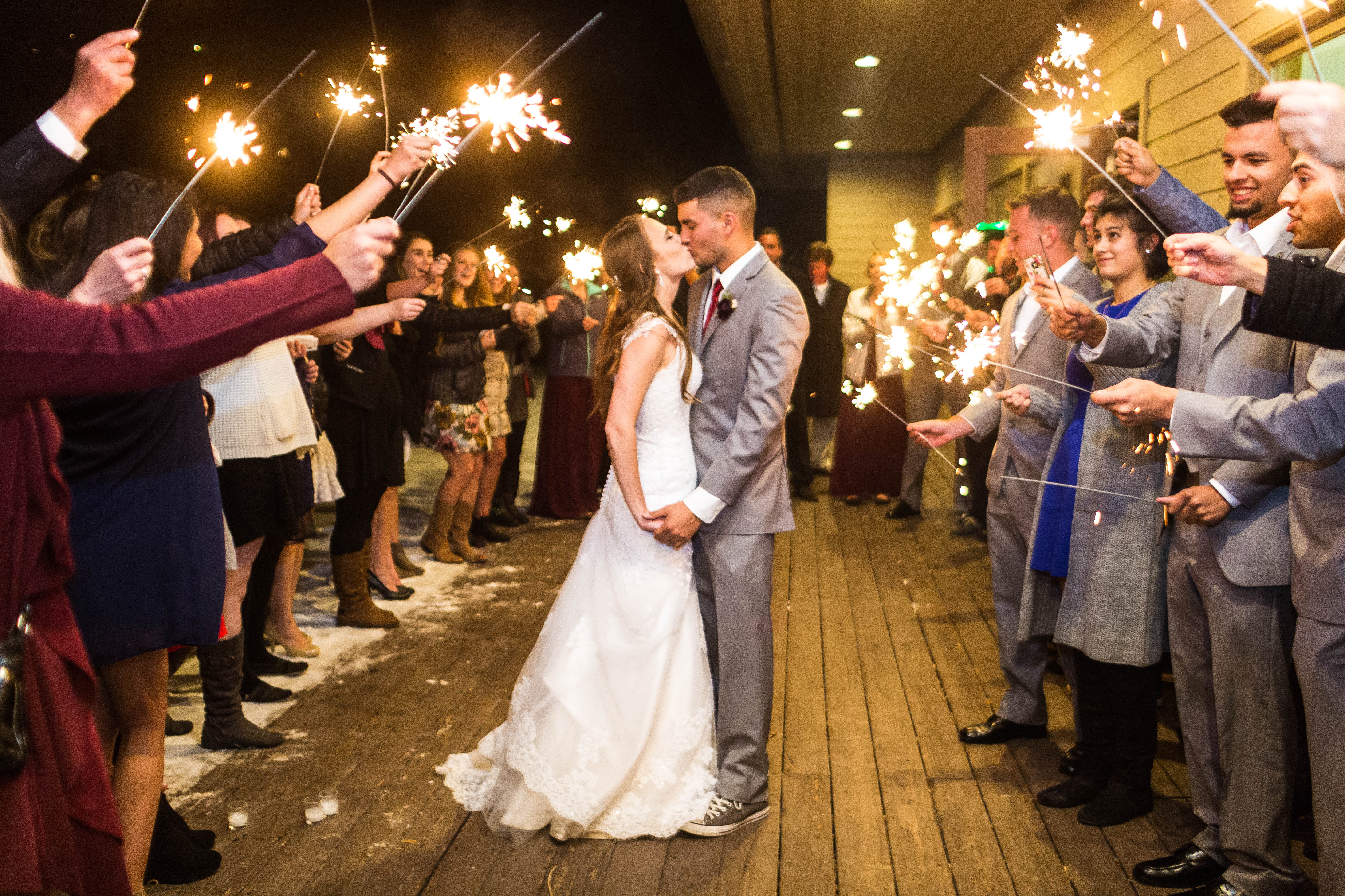 Bride and groom kiss while surrounded by friends and family with sparklers