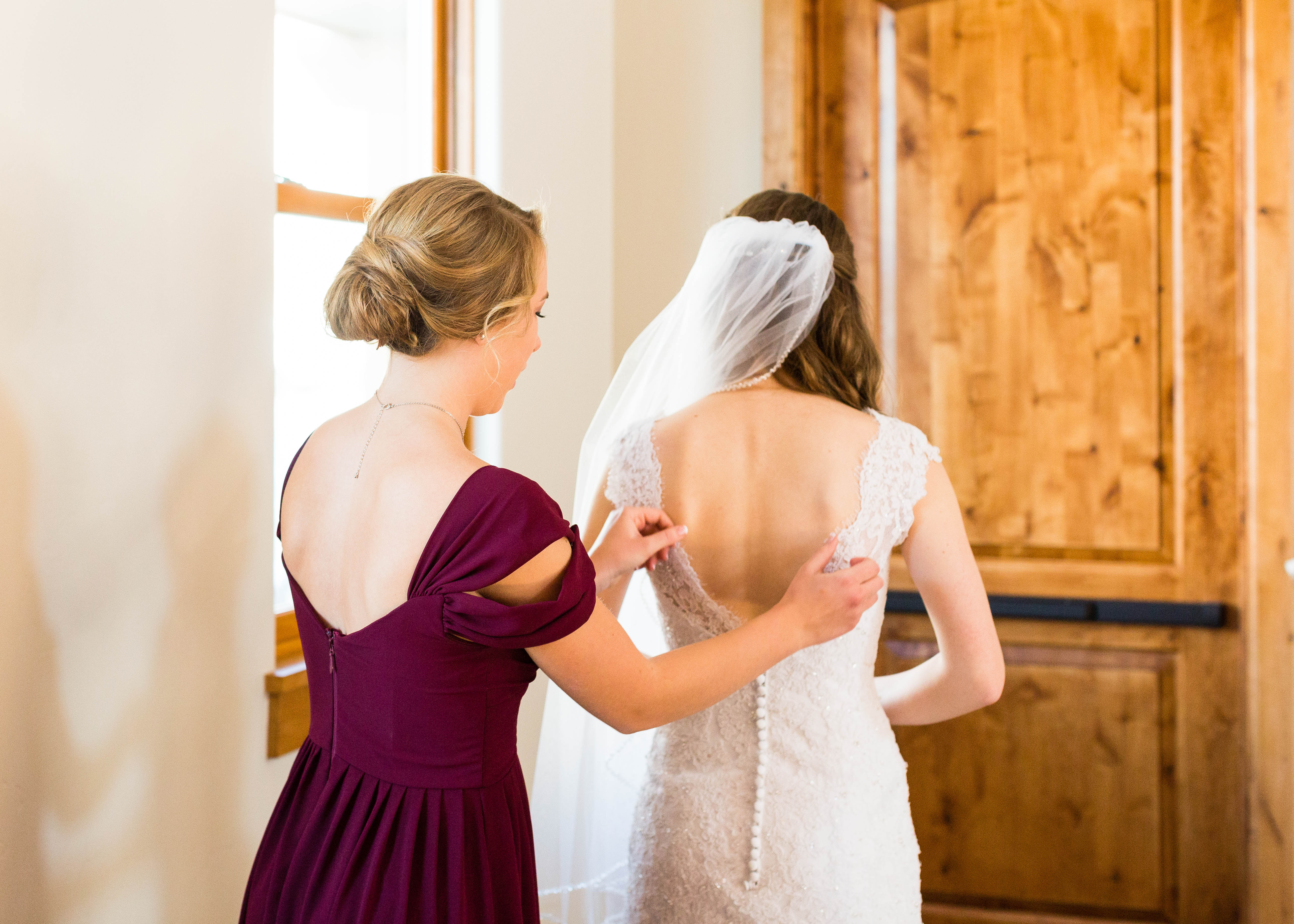 Maid of Honor adjusts the back of the Bride's romantic beaded lace wedding dress