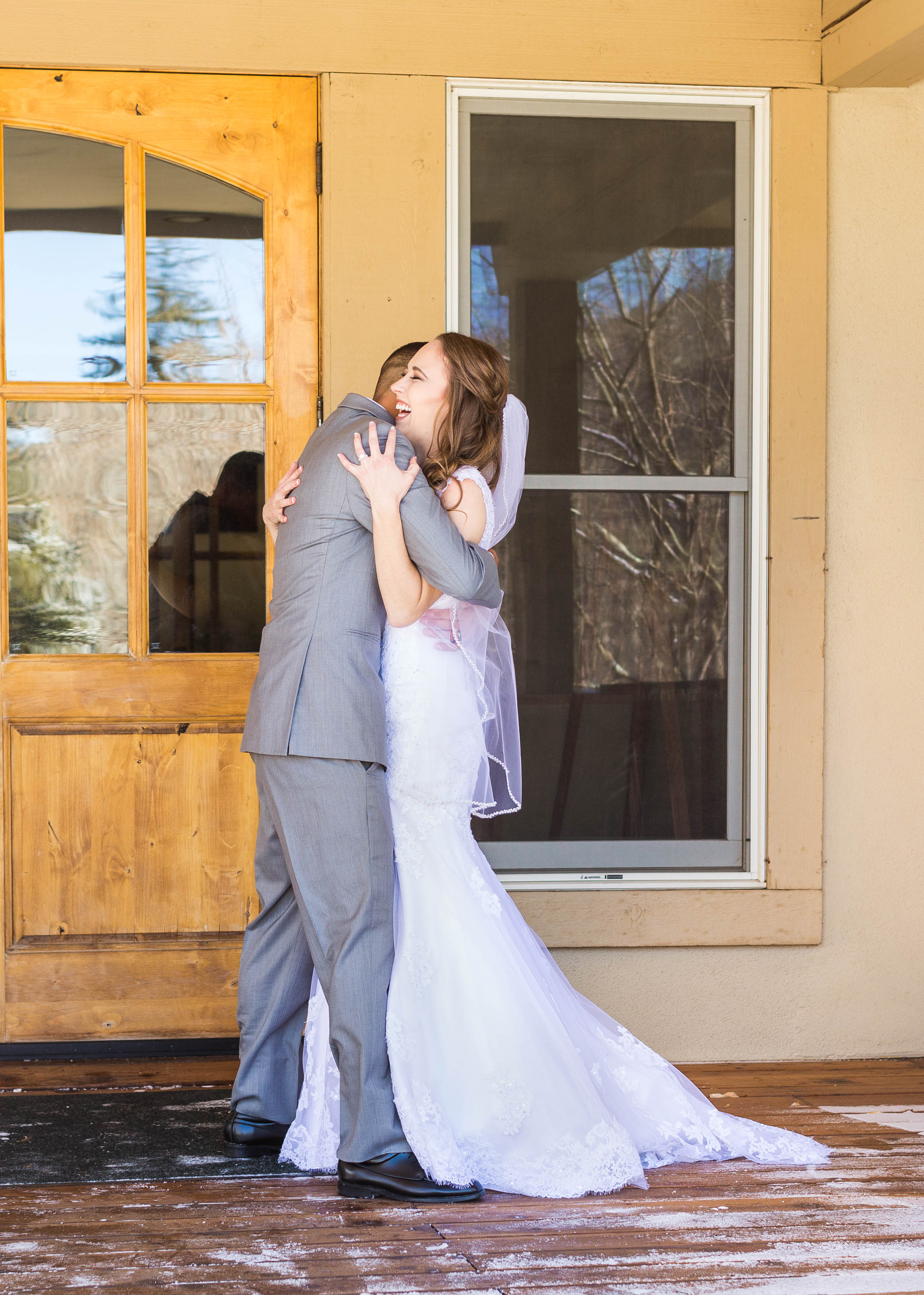 Bride and groom smile and embrace on front porch during their first look