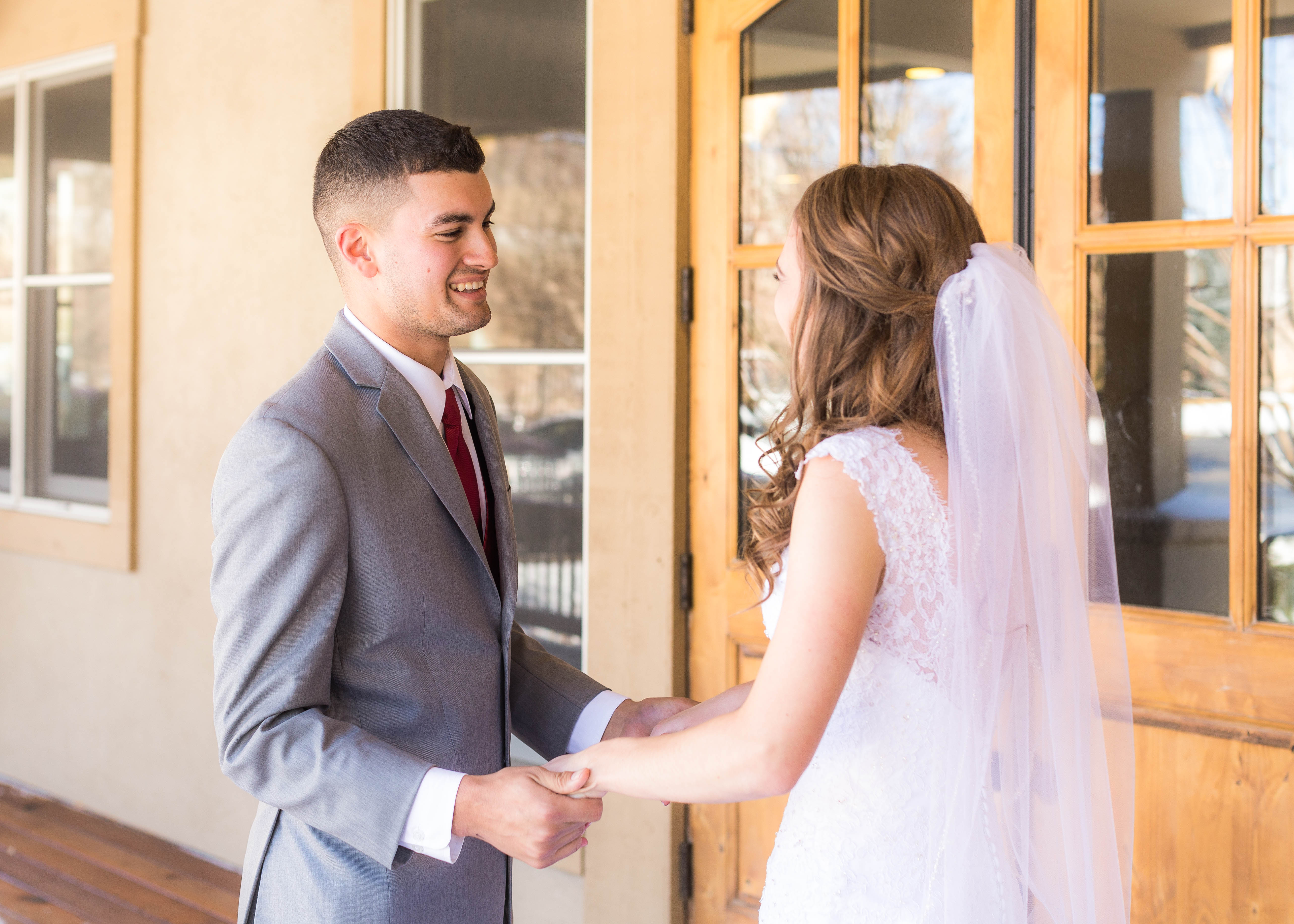 Groom smiles and holds bride's hands as he sees her for the first time on wedding day