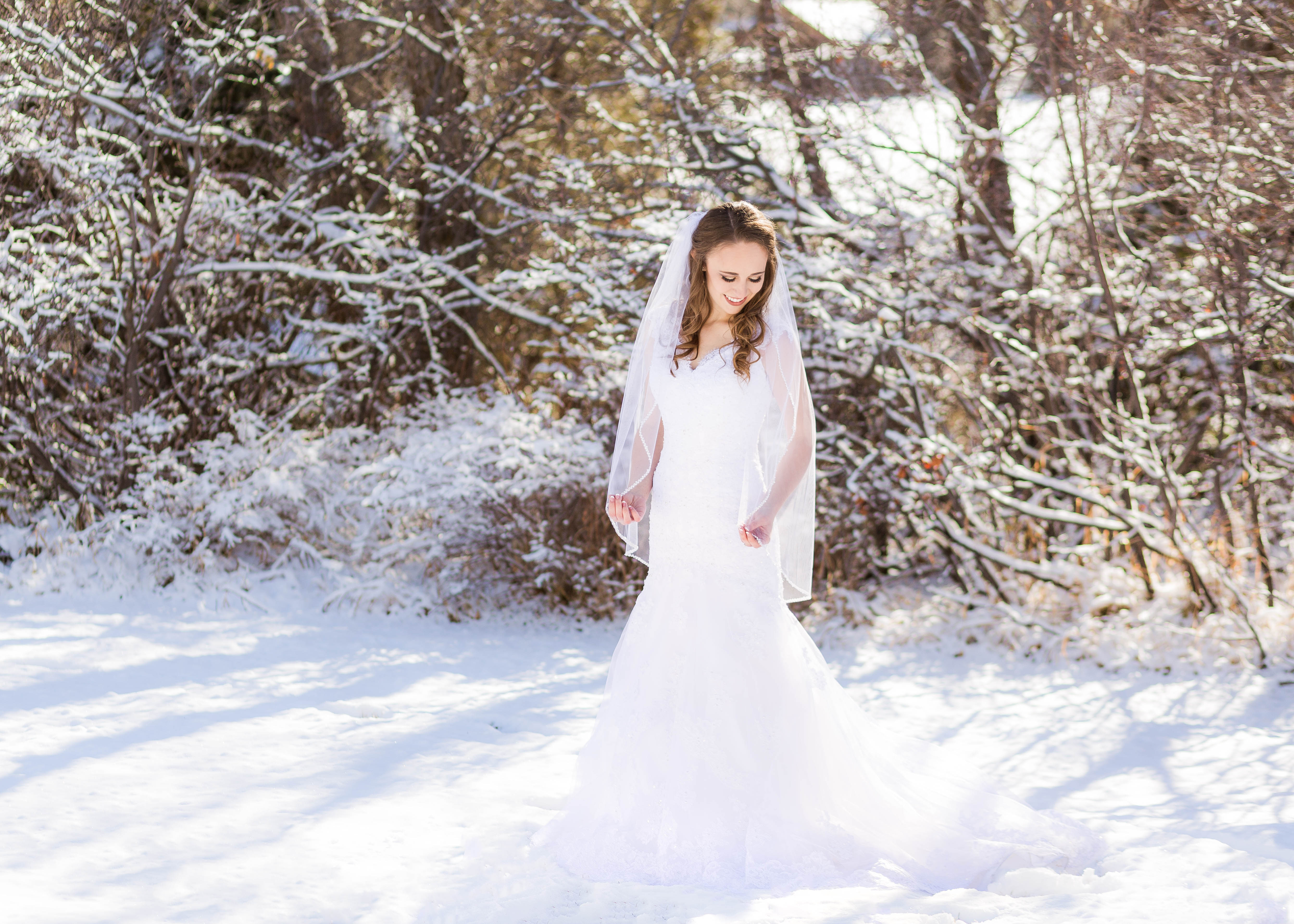 bride looks over her shoulder and grasps edges of veil as she stands in the snow