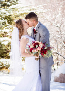 bride and groom kiss surround by trees covered in snow