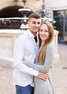 couple hug and smile at the camera in front of an empty fountain on a winter day