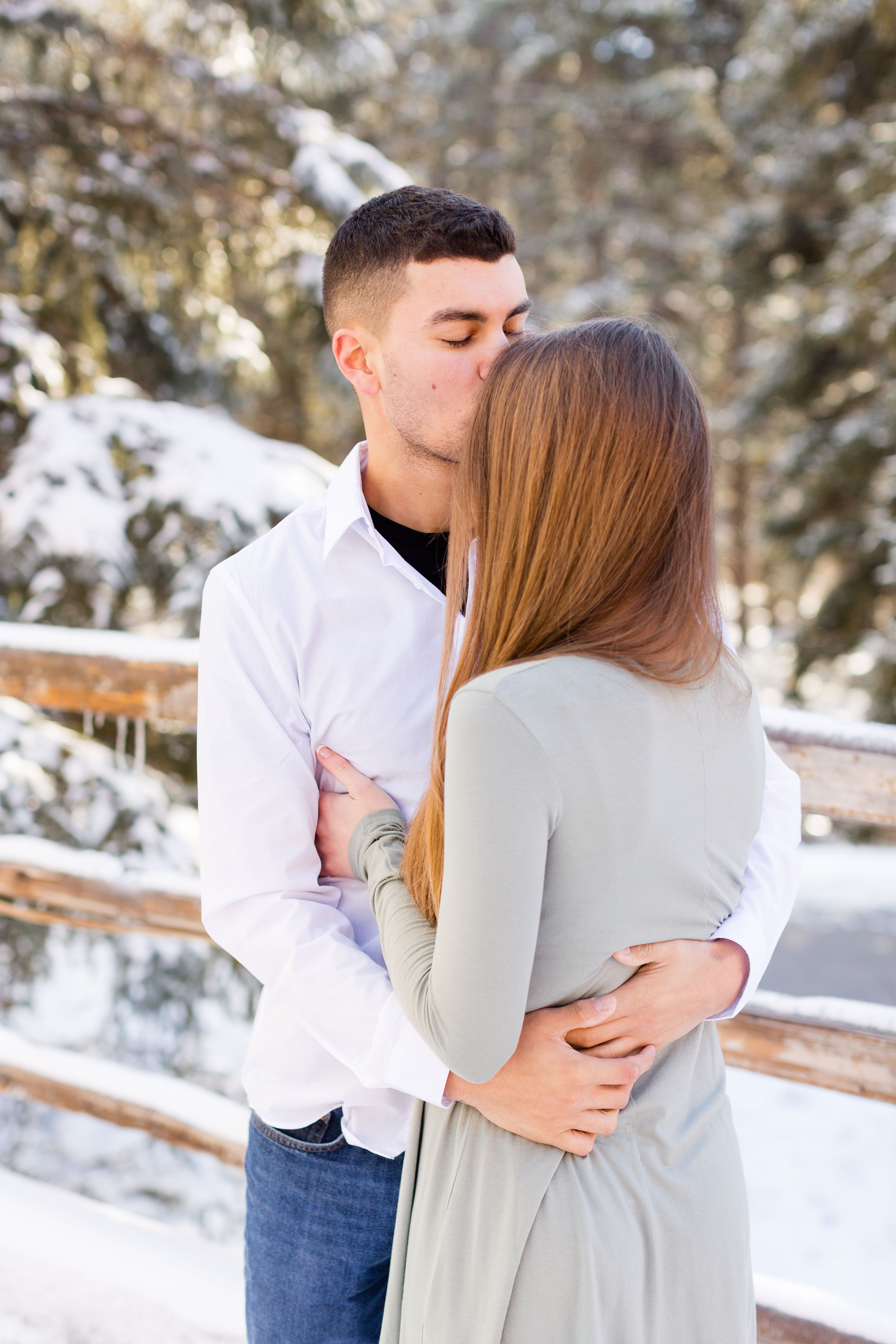 man kisses wife's forehead as he holds her tight on a snowy day
