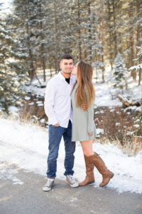 wife gently kisses husband's cheek on a snow covered path in the mountains