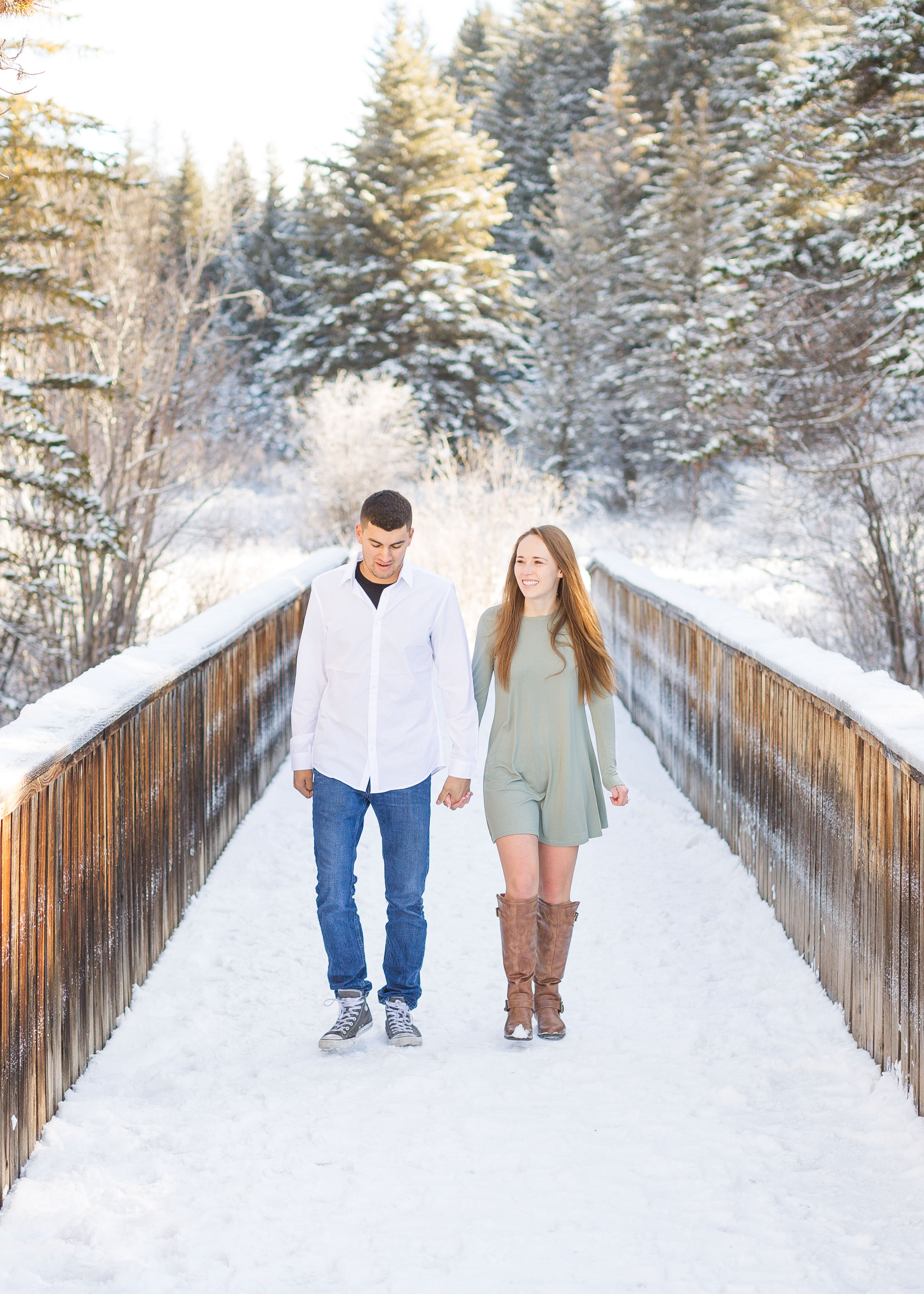 couple hold hands and walk across a snow covered wooden bridge at Vail Ski Resort