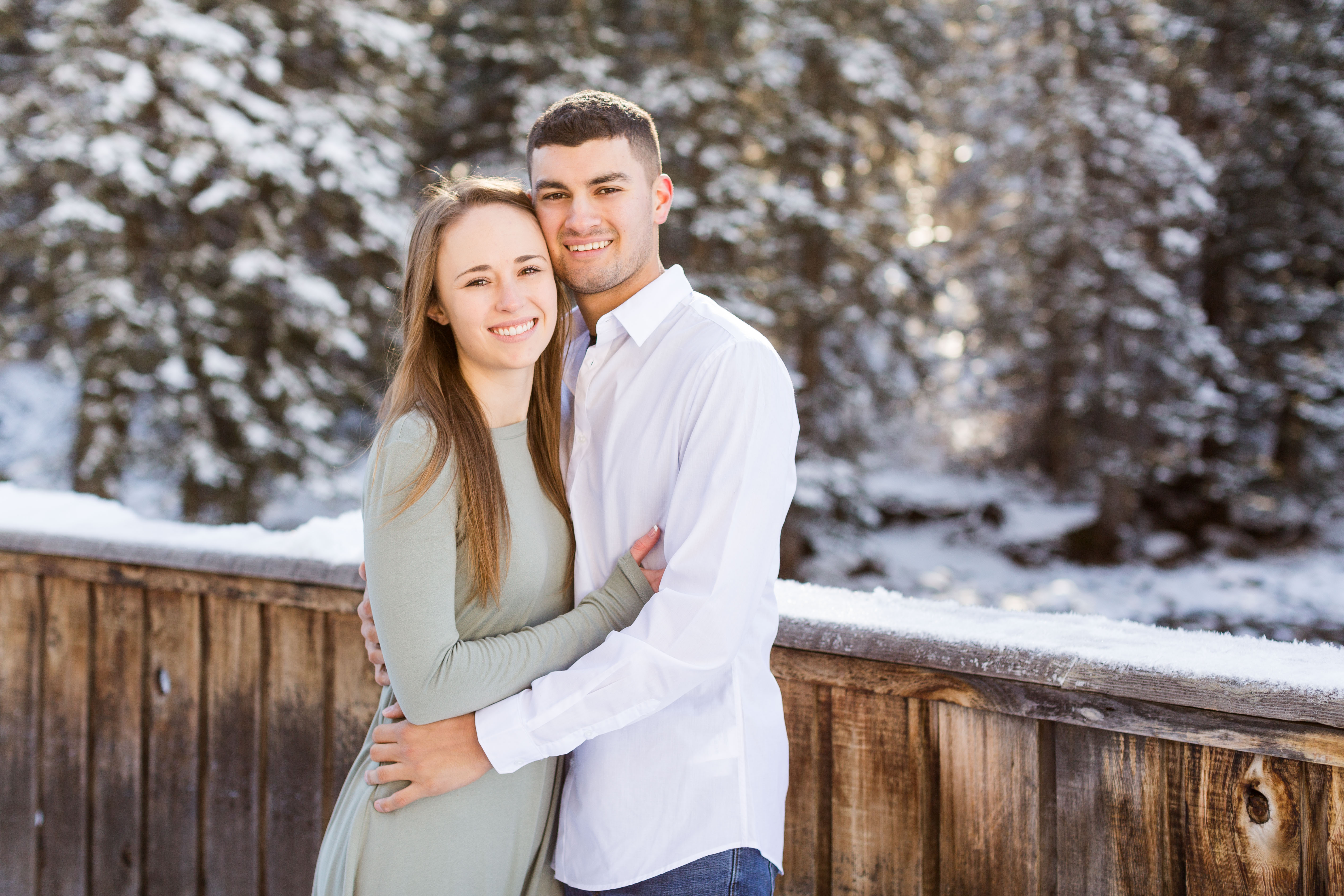 couple hold each other and smile on a wooden bridge on a snowy day