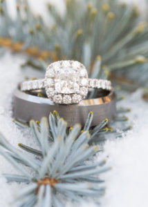 wedding rings sit on a bluish green pine branch in the snow