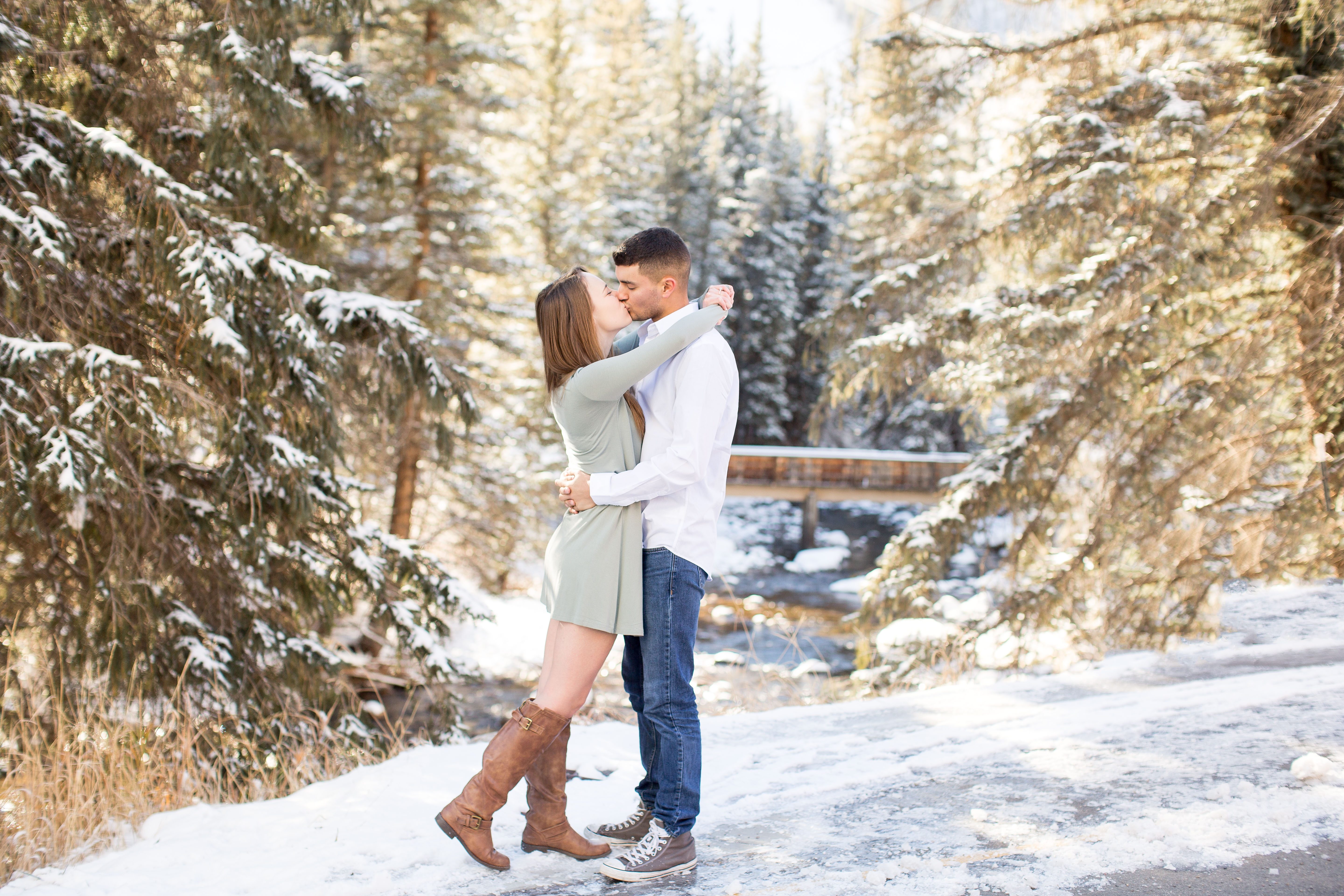 couple embraces in front of snow covered bridge outside of Vail Village