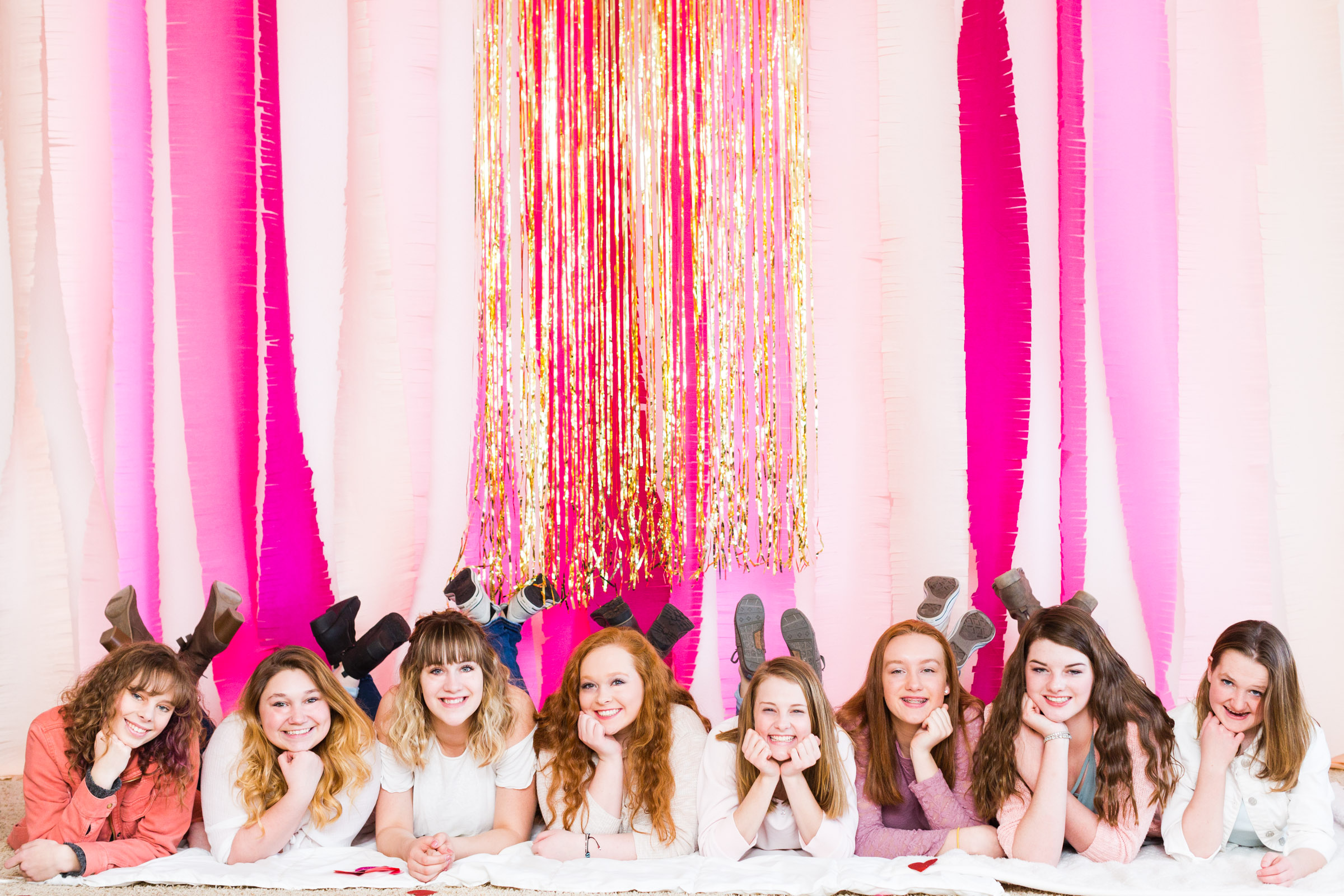 Spokesmodel Team of high school girls smiling and laying on the floor in front of a pink and gold backdrop