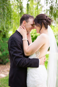 bride and groom press foreheads together and smile in garden