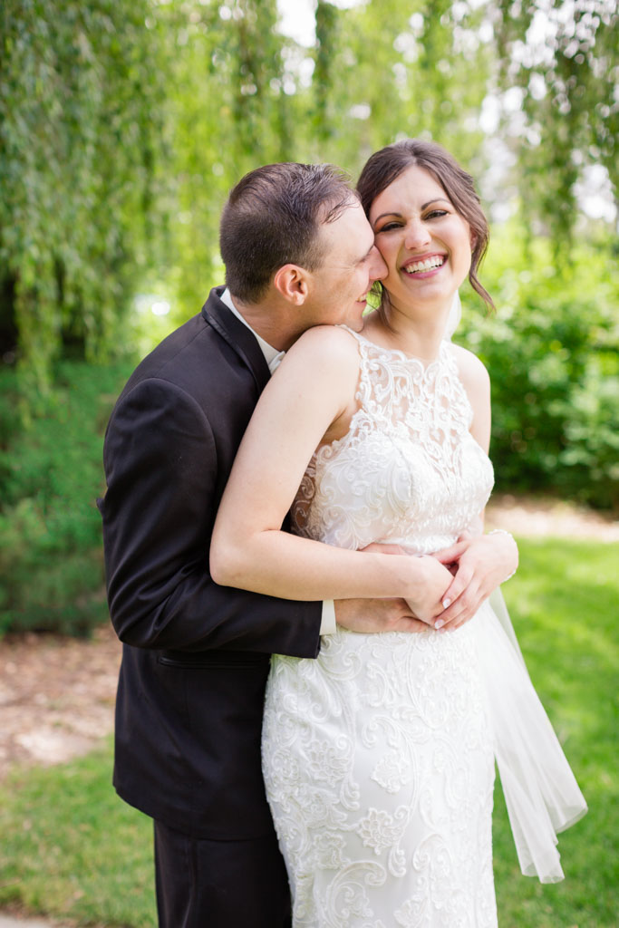 Groom embraces bride from behind and smiles