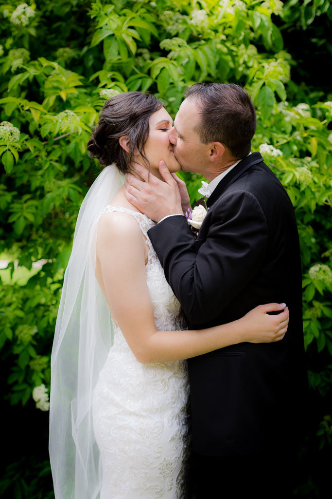bride and groom kiss by a pretty bush